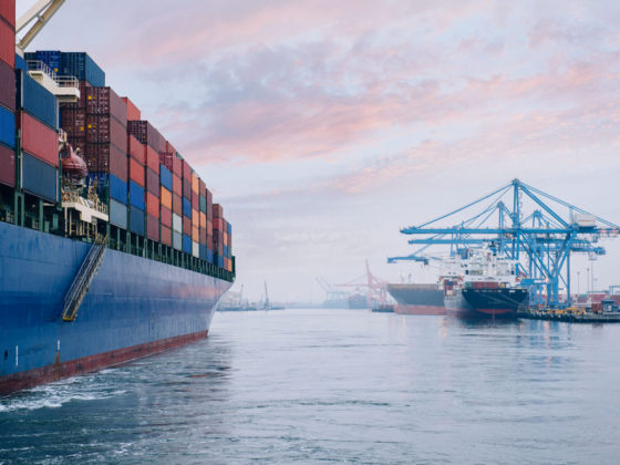 Loaded container ship coming into port with large dock cranes in the background