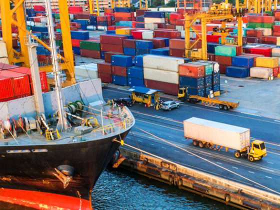 Docked cargo ship with containers in the background and trucking driving away