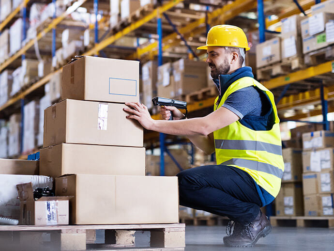 Man in hardhart and safety vest scanning a box in a warehouse