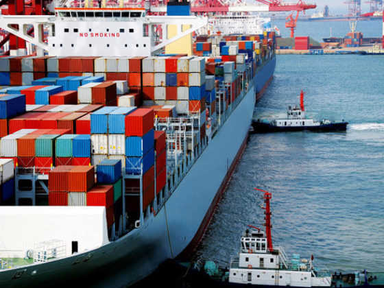 Tugboats pushing cargo ship loaded with containers up to a dock