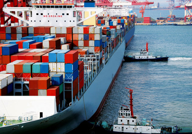 Tugboats pushing cargo ship loaded with containers up to a dock