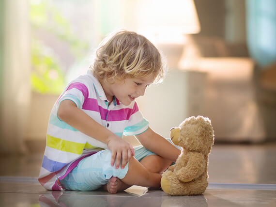 Toddler sitting on the floor looking at a stuffed teddy bear