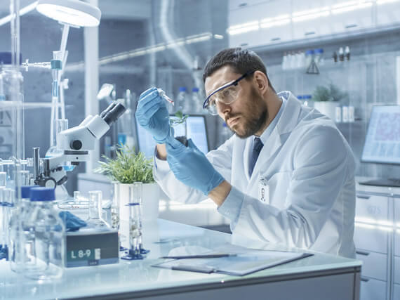 Man in lab coat with gloves and goggles working in a lab